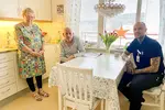 En äldre man och kvinna tillsammans med en man som arbetar inom hemtjänsten, de står och sitter i ett kök
