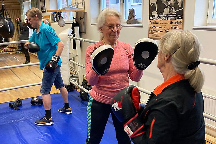 ett par äldre kvinnor står med boxningshandske i en träningslokal